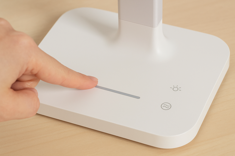 A finger sliding along a touch-sensitive bar on an LED lamp's base to adjust brightness, with color temperature icons nearby