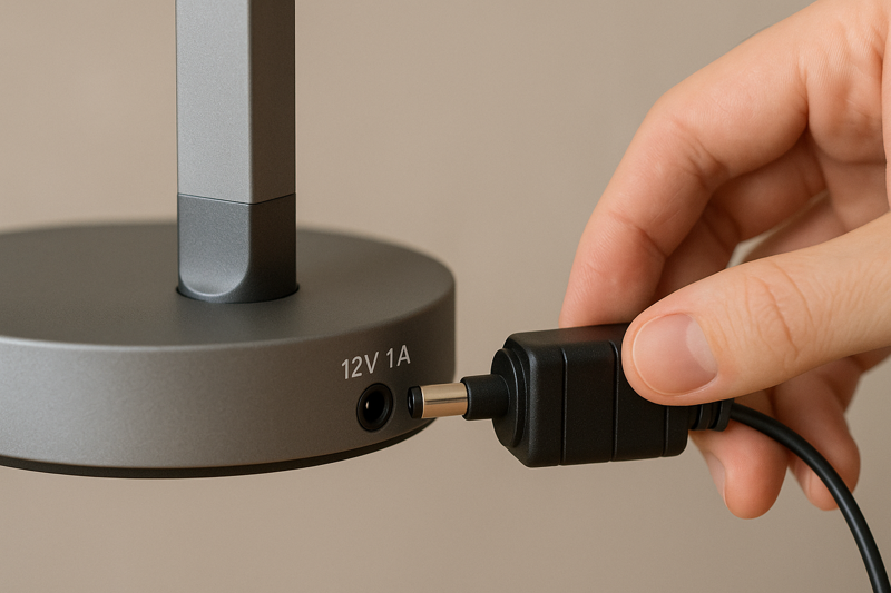 A close-up of the correct power adapter being plugged into the back of an LED desk lamp, with focus on the voltage information