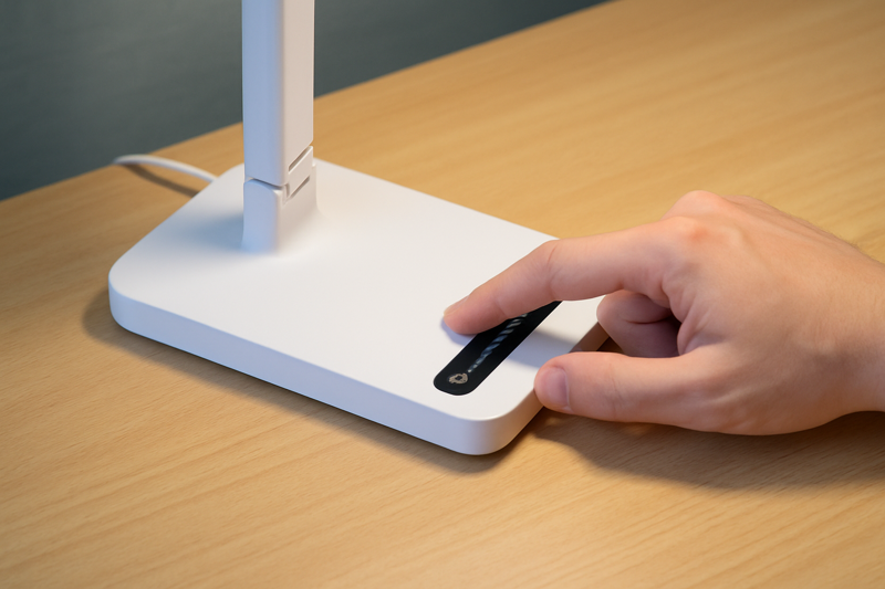 A hand sliding along a touch-sensitive dimmer bar on a desk lamp to adjust the brightness smoothly