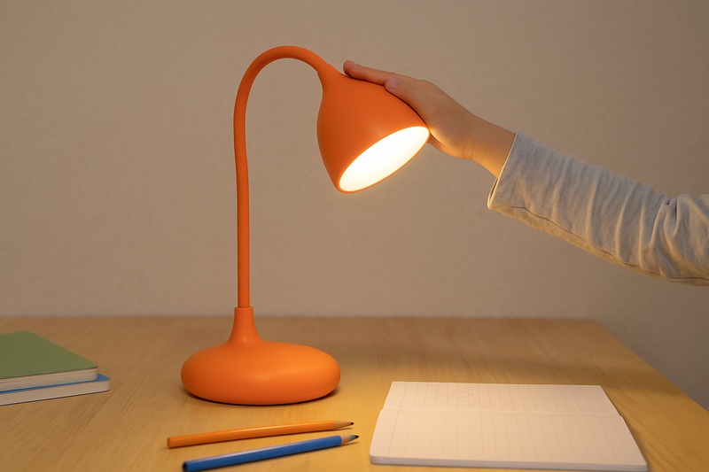 alt text: A sturdy, modern children's lamp with a wide, stable base sitting securely on a desk. The lamp head is made of durable, rounded plastic, and a small hand is touching it safely.